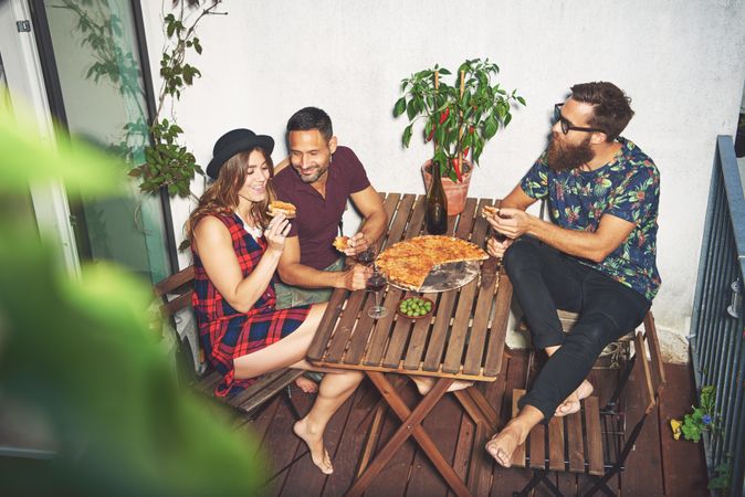 Three friends on a rooftop patio with pizza and wine