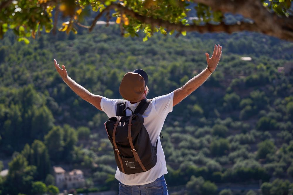 Male traveler with backpack standing in highlands and raising ar