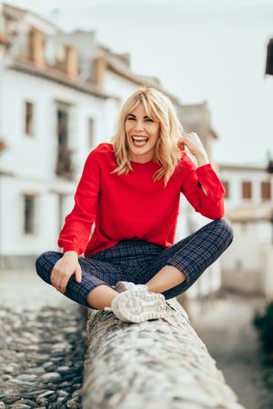 Laughing young blond woman sitting on rocky stoop in Spanish town