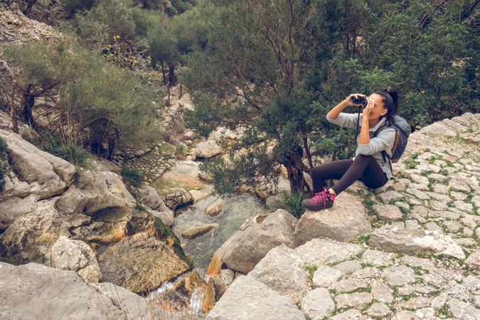 Female traveler on edge of cliff and looking in binoculars