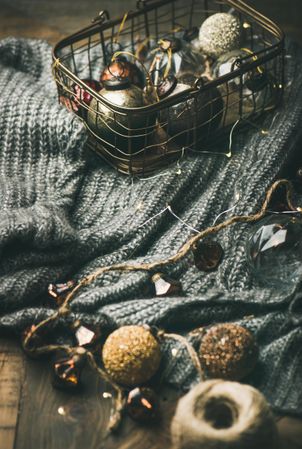 Festive decorations in wire box arranged around grey woolen sweater with yarn and garland