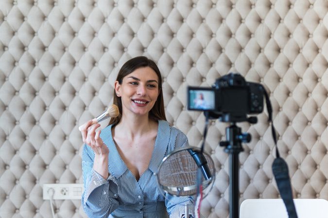 Happy woman applying powder and recording video on camera