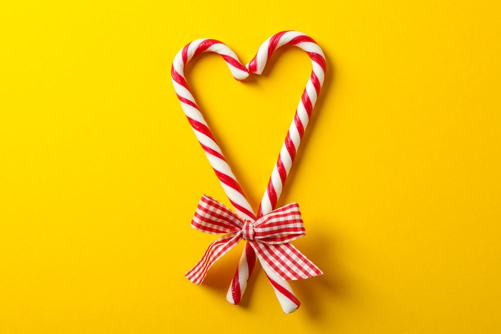 Sweet candy canes with bow on yellow background, space for text