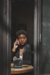 Serious stylish Black woman talking on smartphone in cafe