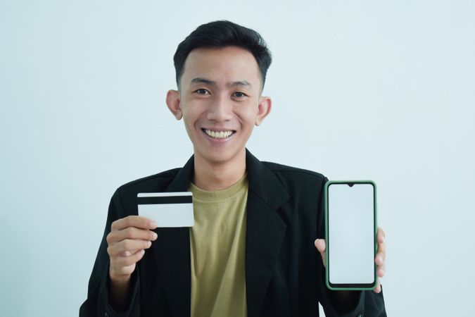 Happy Asian businessman in suit holding blank credit card and smartphone