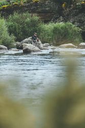 Confident man fishing with rod while standing in river stream