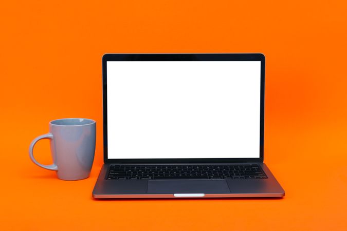 Laptop with mockup screen with cup of coffee or tea in orange studio shoot