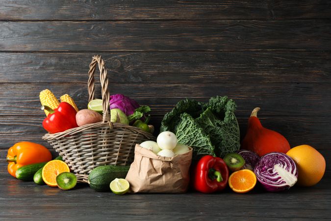 Vegetables, fruits, wicker basket and paper bag on wood background, copy space