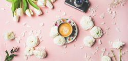 Coffee, camera, tulips artfully arranged on pink background, wide composition