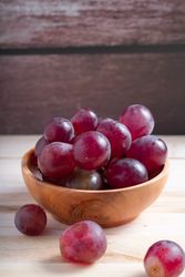 A bowl of red grapes sits on a wooden table