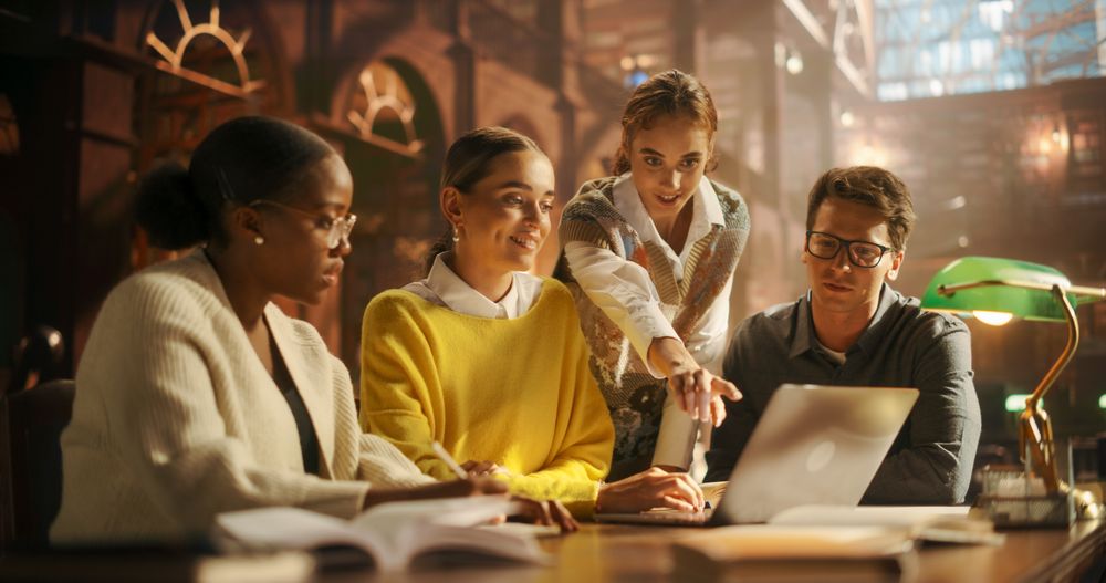 Diverse Group of Students Collaborating on a Project in a Library, Using Laptop for Research.