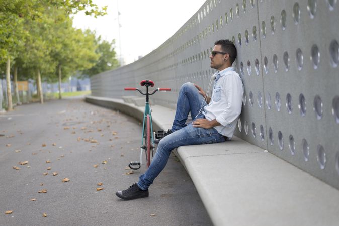 Male in sunglasses relaxing outside of park with bicycle