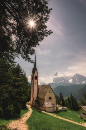 Small church on hilly valley in forest with bright sun lights penetrating foliage