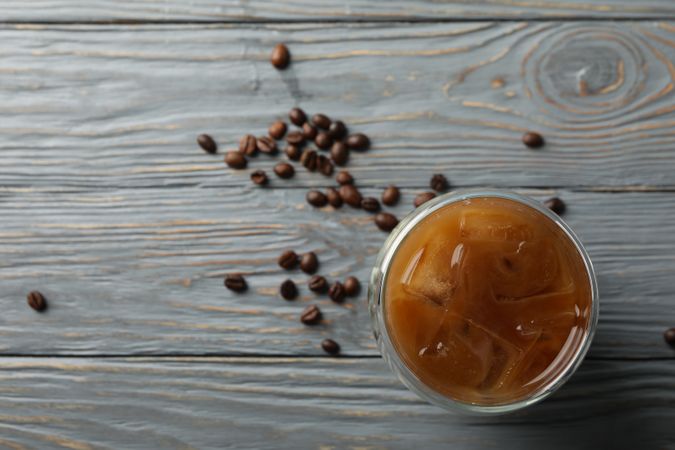 Glass of ice coffee on wooden background. Coffee seeds