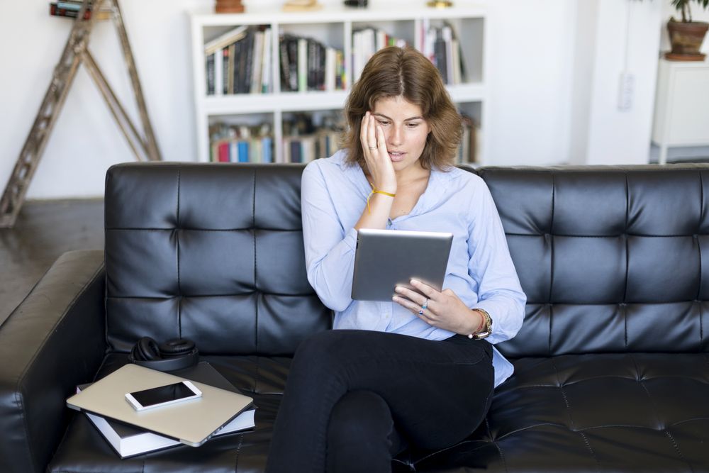 Female sitting on couch at home and shocked by something on a digital tablet