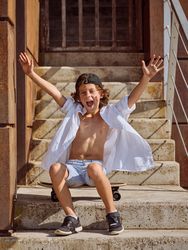 Cheerful boy in summer outfit with raised hands sitting on stair