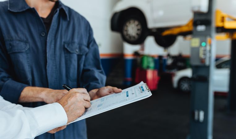 Mechanic taking signature on document from customer in garage