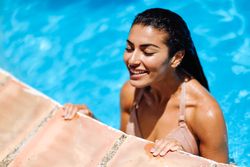 Beautiful Arab woman grasping side of swimming pool with eyes closed on sunny day