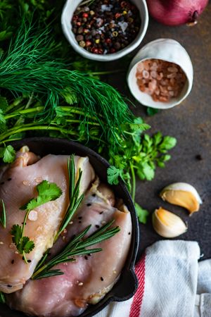 Raw chicken with rosemary sprig on kitchen slab with seasoning and herbs