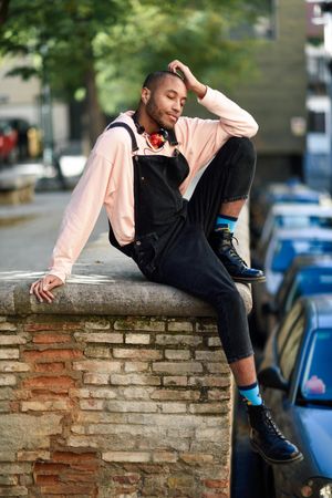 Calm male sitting with one leg up on brick wall in city with eyes closed