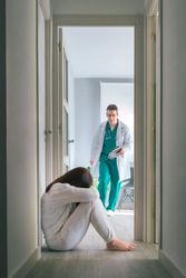 Worried physician running to help patient sitting on floor in mental health center