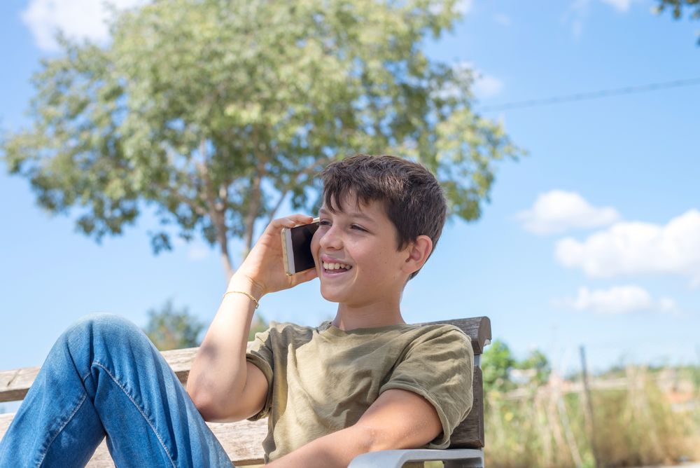 Smiling boy sitting on bench talking on phone