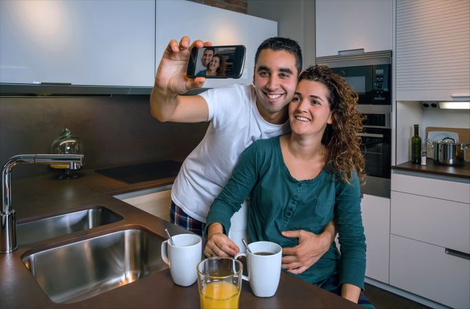 Cute couple in pajamas taking selfie in kitchen at breakfast time