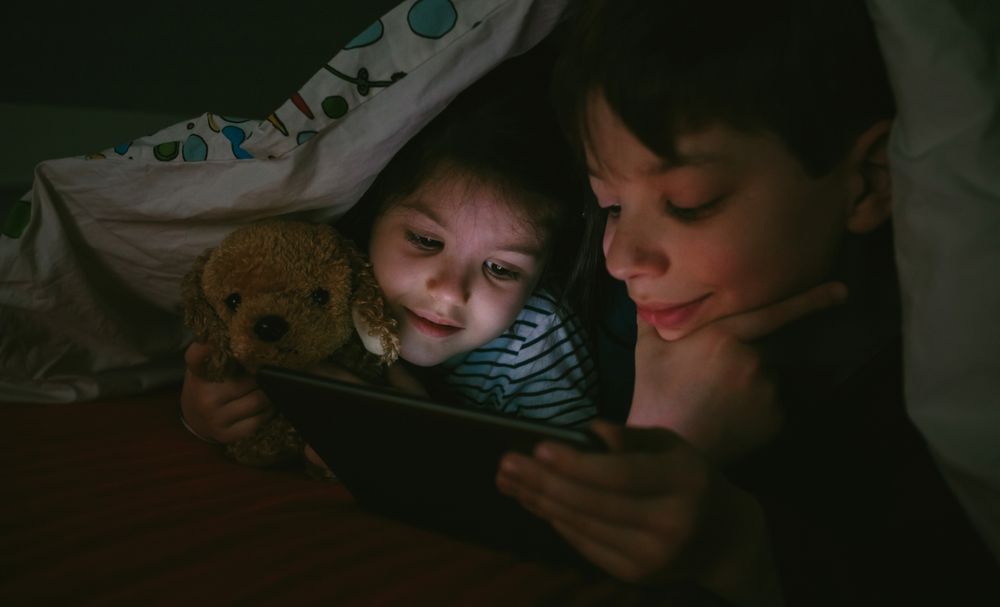 Siblings looking at the tablet in the dark