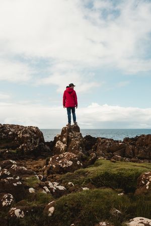 Lonely tourist standing on rocky coast against tranquil sea water under gray sky