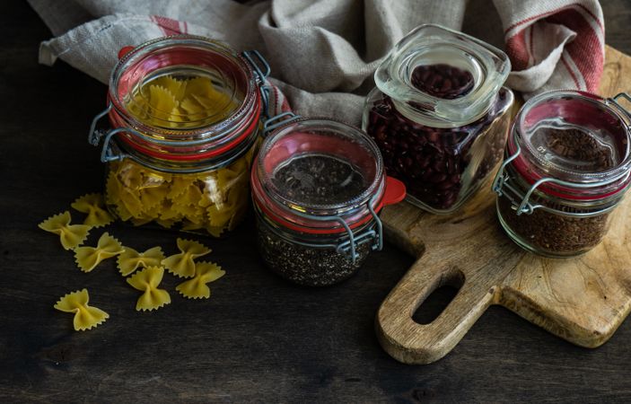 Ingredients in glass containers with pasta, seeds and beans on wooden background with copy space