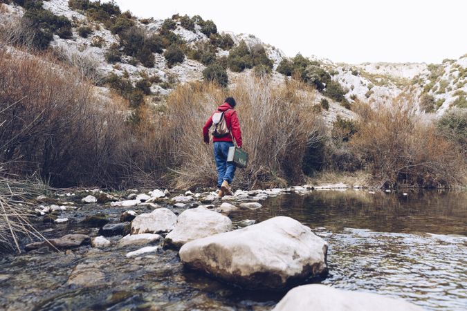 Woman with case jumping on rocks above stream