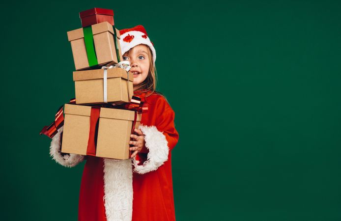 Little girl in Santa Claus costume holding a pile of gift boxes