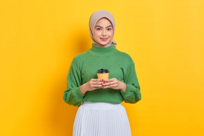 Woman in headscarf holding to go coffee cup with both hands