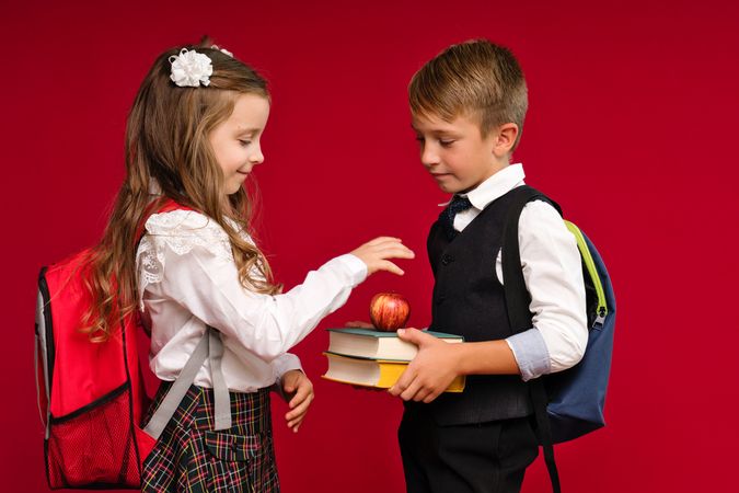 Preteens in school uniform carry backpacks on vivid red colored background