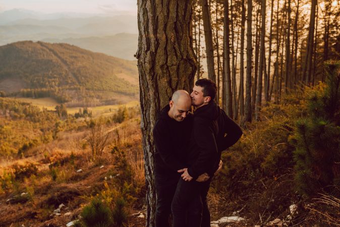 Smiling men hugging near tree in forest on hill