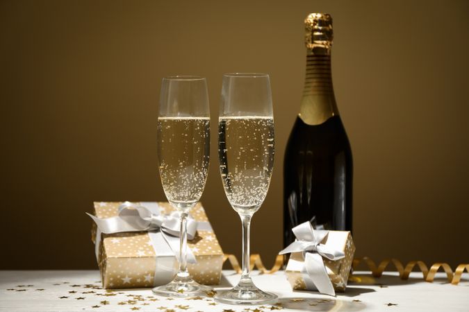 Gifts, champagne glasses and bottle on golden background, space for text
