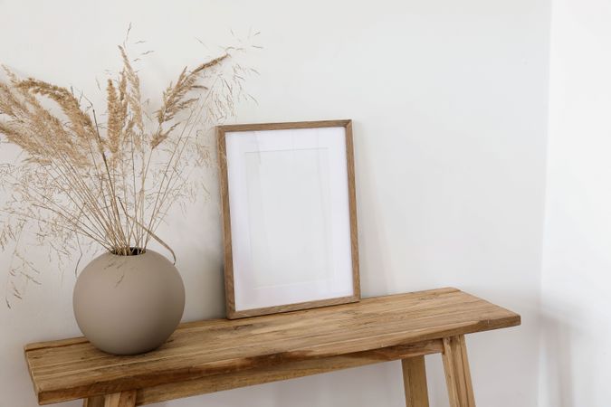 Modern interior. Beige ball vase with dray bunny tail, festuca grass. Blank vertical wooden frame picture mock up on old wooden table, bench
