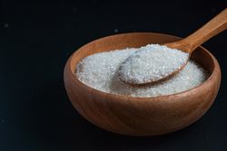 granulated sugar in a wooden bowl with a wooden spoon full of sugar on top