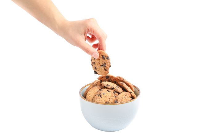 Young woman holding tasty chocolate chip cookie over bowl on studio background, closeup