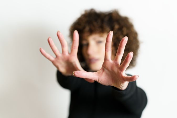 Blurred woman in dark sweater looking through two hands with palms to the camera