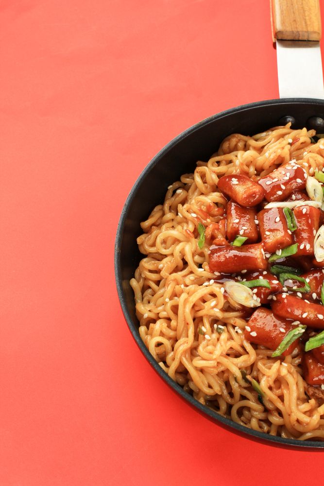 Pan of noodles topped with Korean rice cakes in red studio
