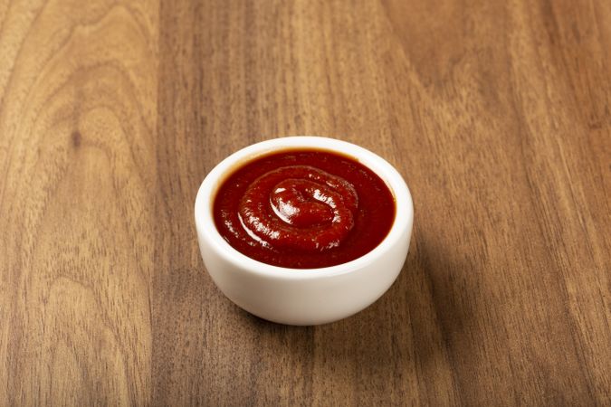 Tomato ketchup in the ramekin on wooden background.