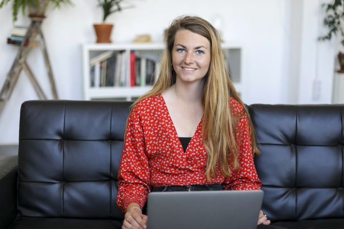 Smiling woman sitting on a sofa at home using a laptop