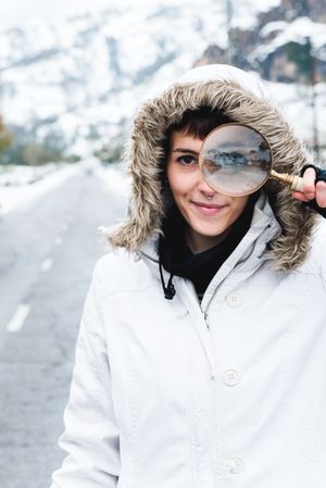 Smiling woman looking through magnifier in winter