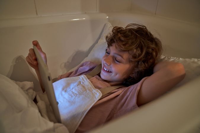 Positive boy watching video on tablet in bathtub