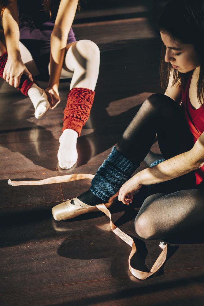 Young ballerinas wearing and lacing white pointe shoes in studio.