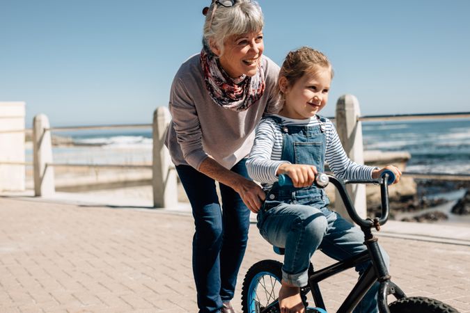 Girl trying to ride a bicycle with the help of her grandmother at seaside promenade