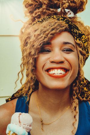 Vertical shot of happy Black female smiling with an ice cream cone in the sun
