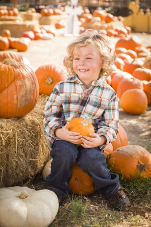 Little Boy Sitting and Holding His Pumpkin at Pumpkin Patch.