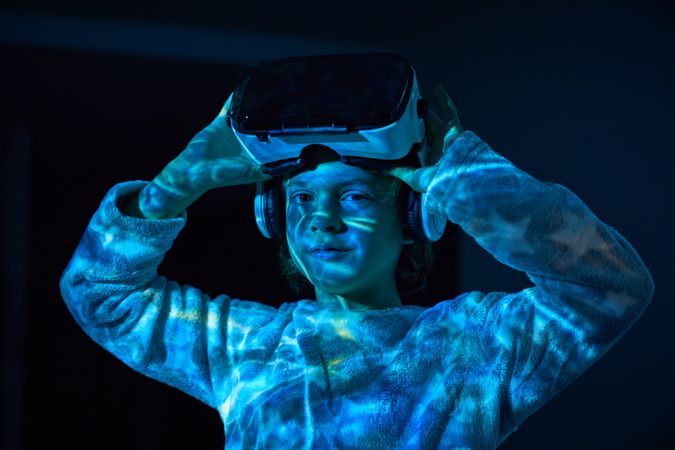 Little boy adjusting VR headset and looking at camera in darknes